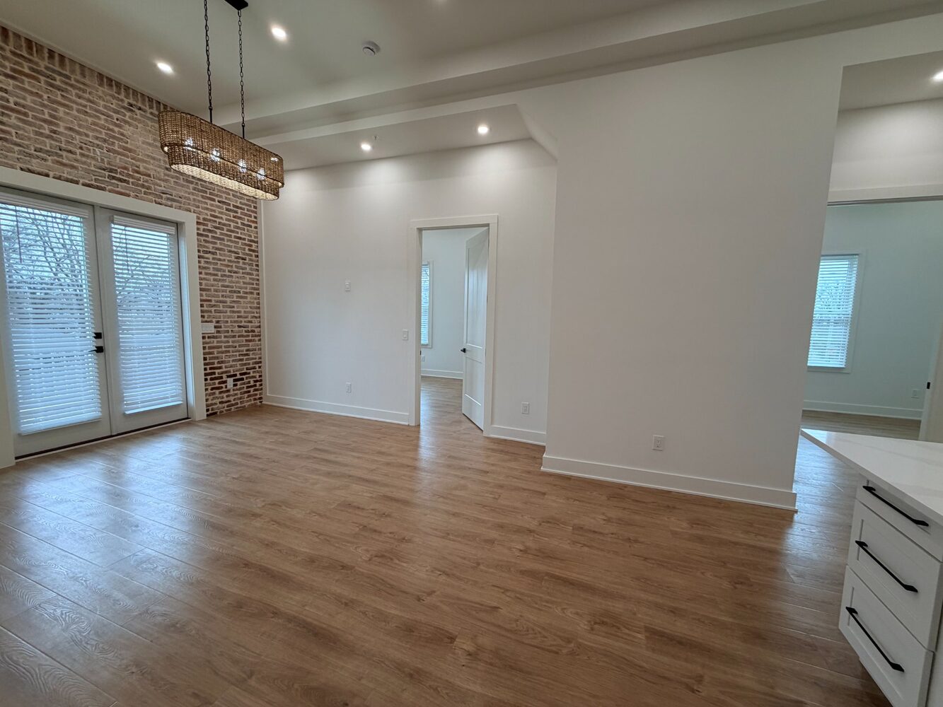 Living room with exposed brick wall, French doors, and woven chandelier
